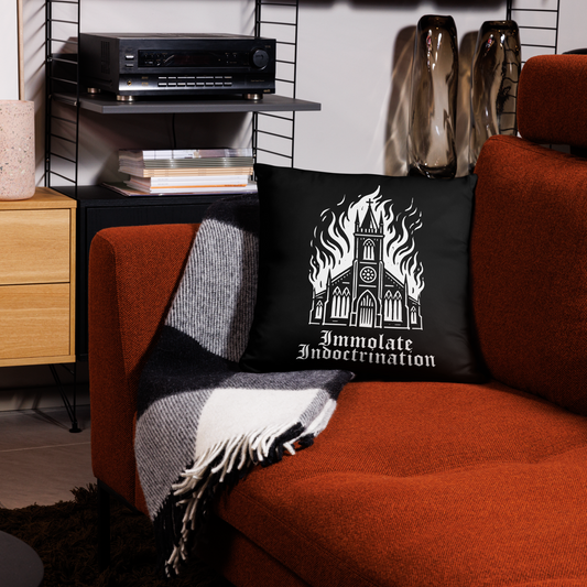 Black square pillow with white design of an illustrated burning church with the words immolate indoctrination in older goth font below