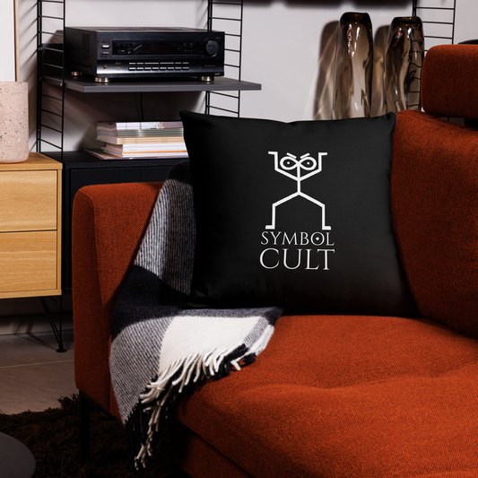 Symbol Cult Logo on a pillow the logo looks like an archic cave drawing of a humanoid figure with an infinity symbol for its head and dots in the symbol for pupils. it also has furrowed eyebrows that look to judge. below are the words Symbol Cult and the O in symbol is the alchemical symbol for the sun. all in white on black