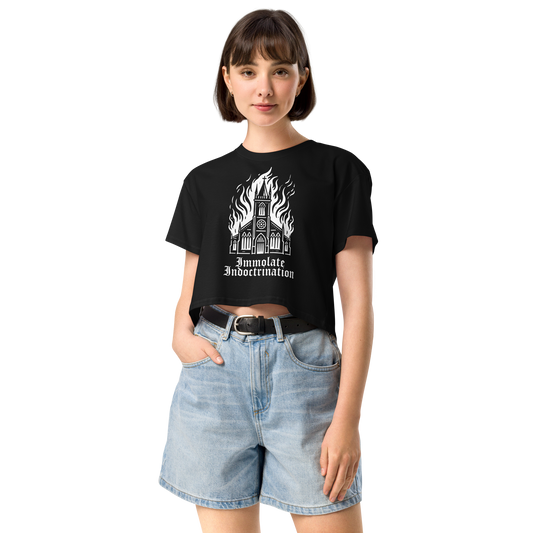 white design on black womens croptop of an illustrated burning church with the words immolate indoctrination in older goth font below
shown on a thin framed woman